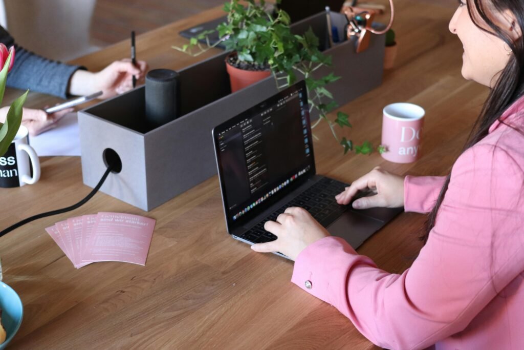 Two women collaborating in a modern office setting with laptops and coffee mugs, highlighting teamwork and technology.