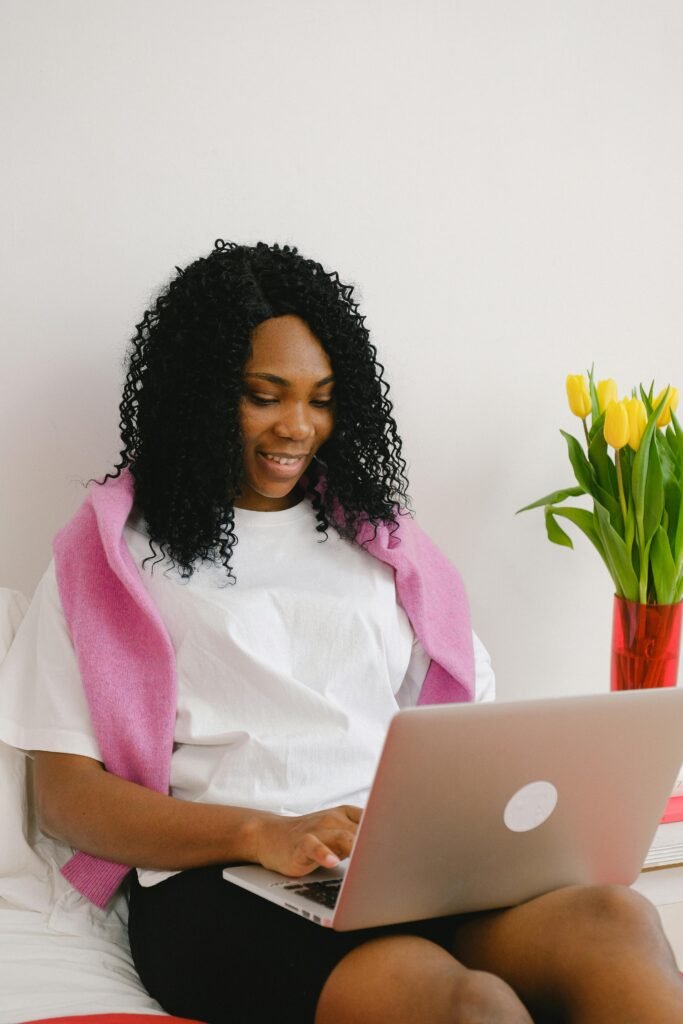 pexels-photo-7191955-7191955-1 A cheerful African American woman using a laptop indoors next to vibrant tulips.