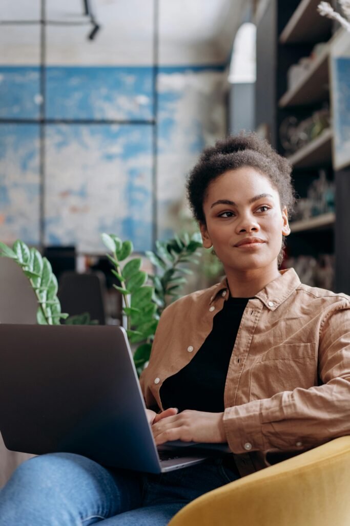 A young woman with curly hair intently works on her laptop in a stylish office environment.